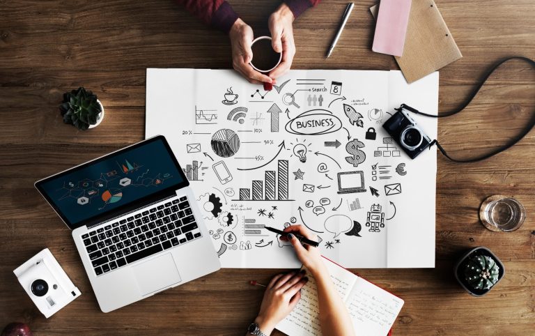 deux personnes qui travaillent sur un plan marketing avec ordinateur, stylos, carnets, feuilles et café