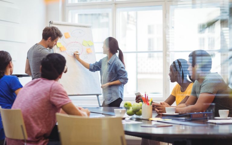 Une équipe attentive aux échange avec une formatrice. Une méthode intéractive avec des post-its sur le paperboard